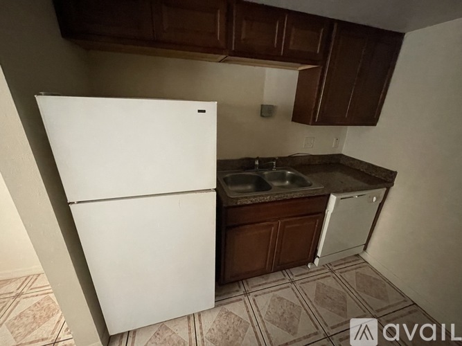 A white refrigerator is in a kitchen with brown cabinets and a tiled floor.