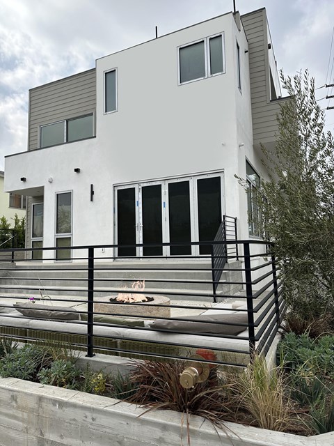 A modern white house with black railings and a black dog on the steps.