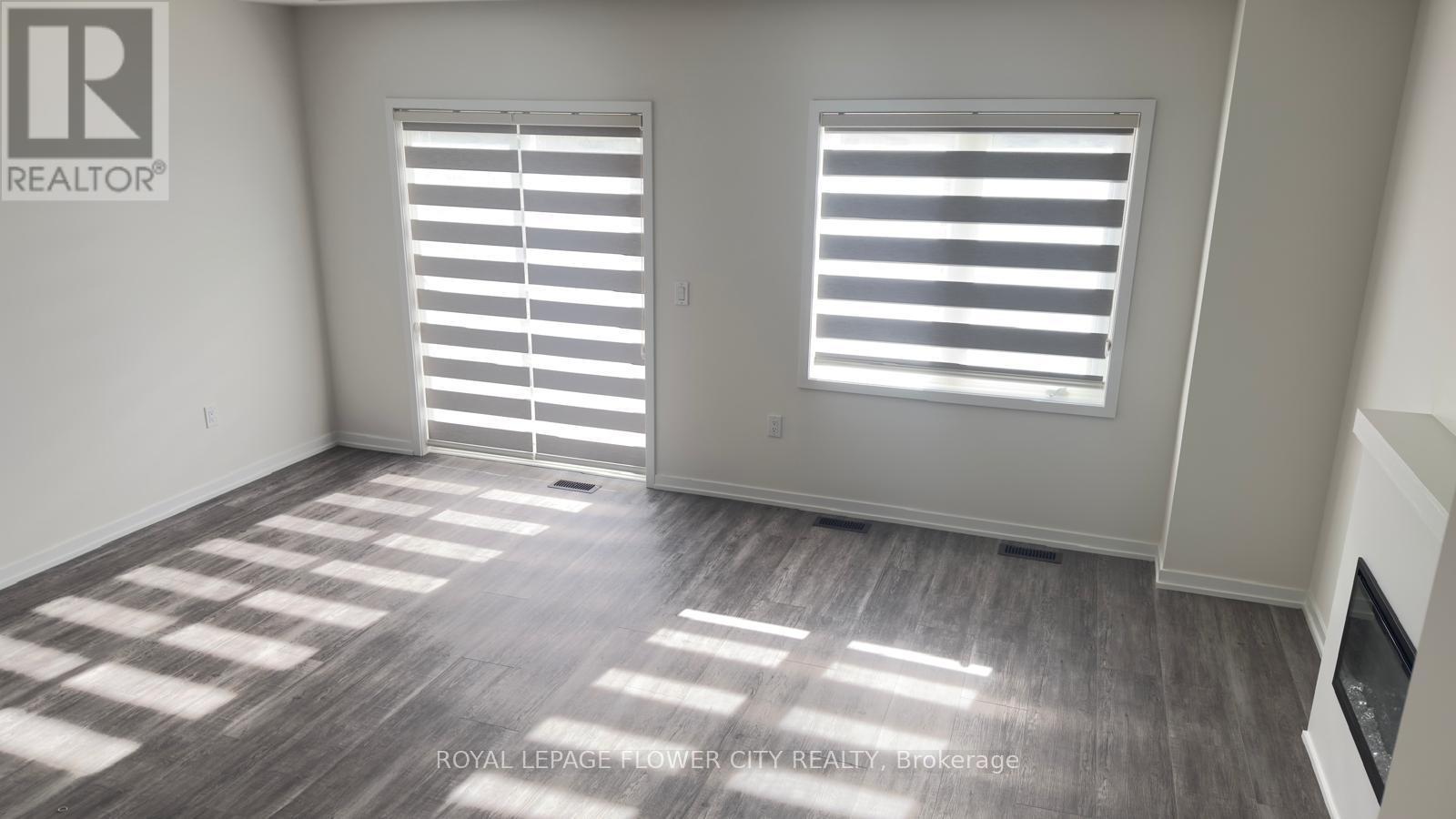 A room with a wooden floor and two windows with blinds.