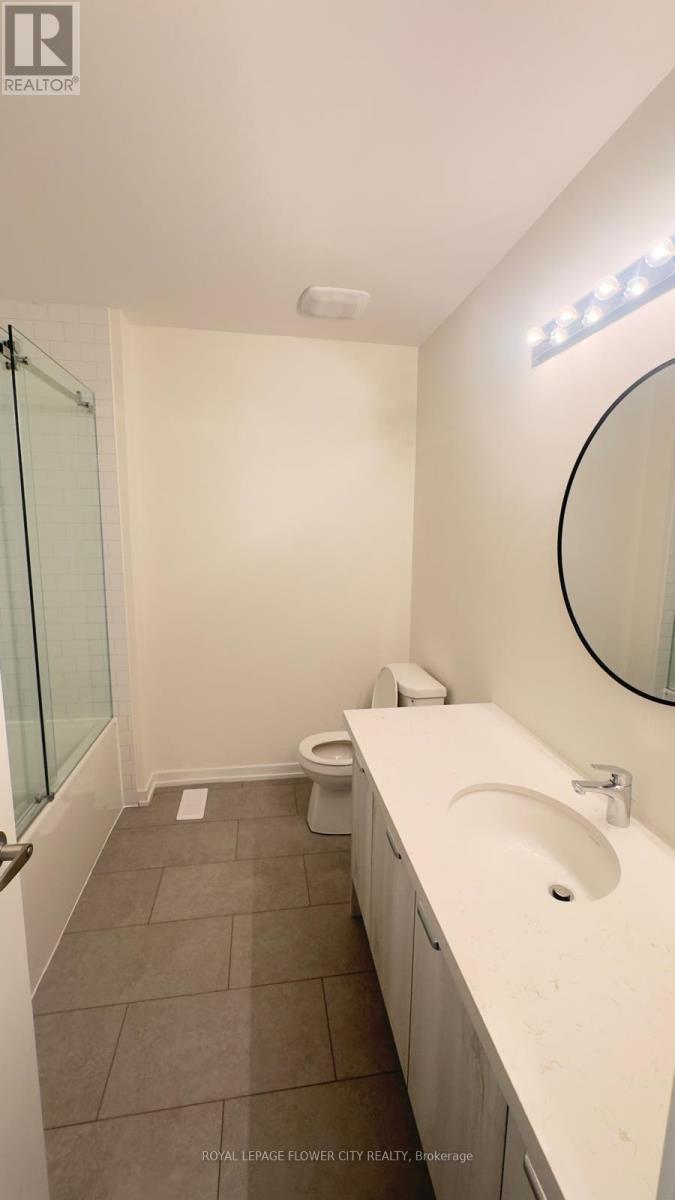 A white sink in a bathroom with a round mirror and a toilet in the corner.
