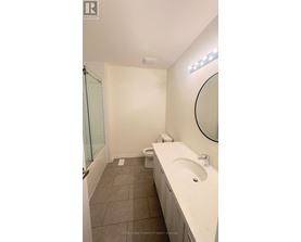 A white sink in a bathroom with a round mirror and a toilet in the corner.