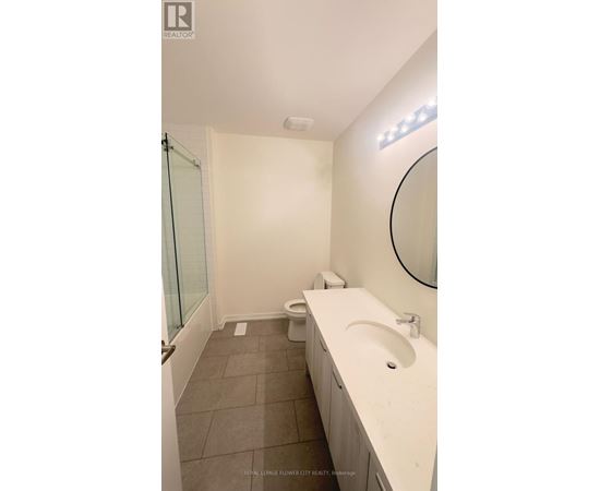 A white sink in a bathroom with a round mirror and a toilet in the corner.