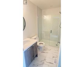 A white toilet sits in a bathroom with a walk-in shower.