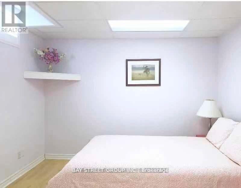 A bedroom with a bed, a lamp, a picture on the wall, and a shelf with a flower arrangement.
