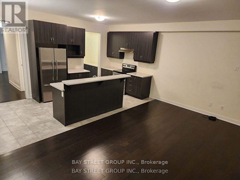 A kitchen with dark wood floors and cabinets, a refrigerator, a sink, and a stove top oven.
