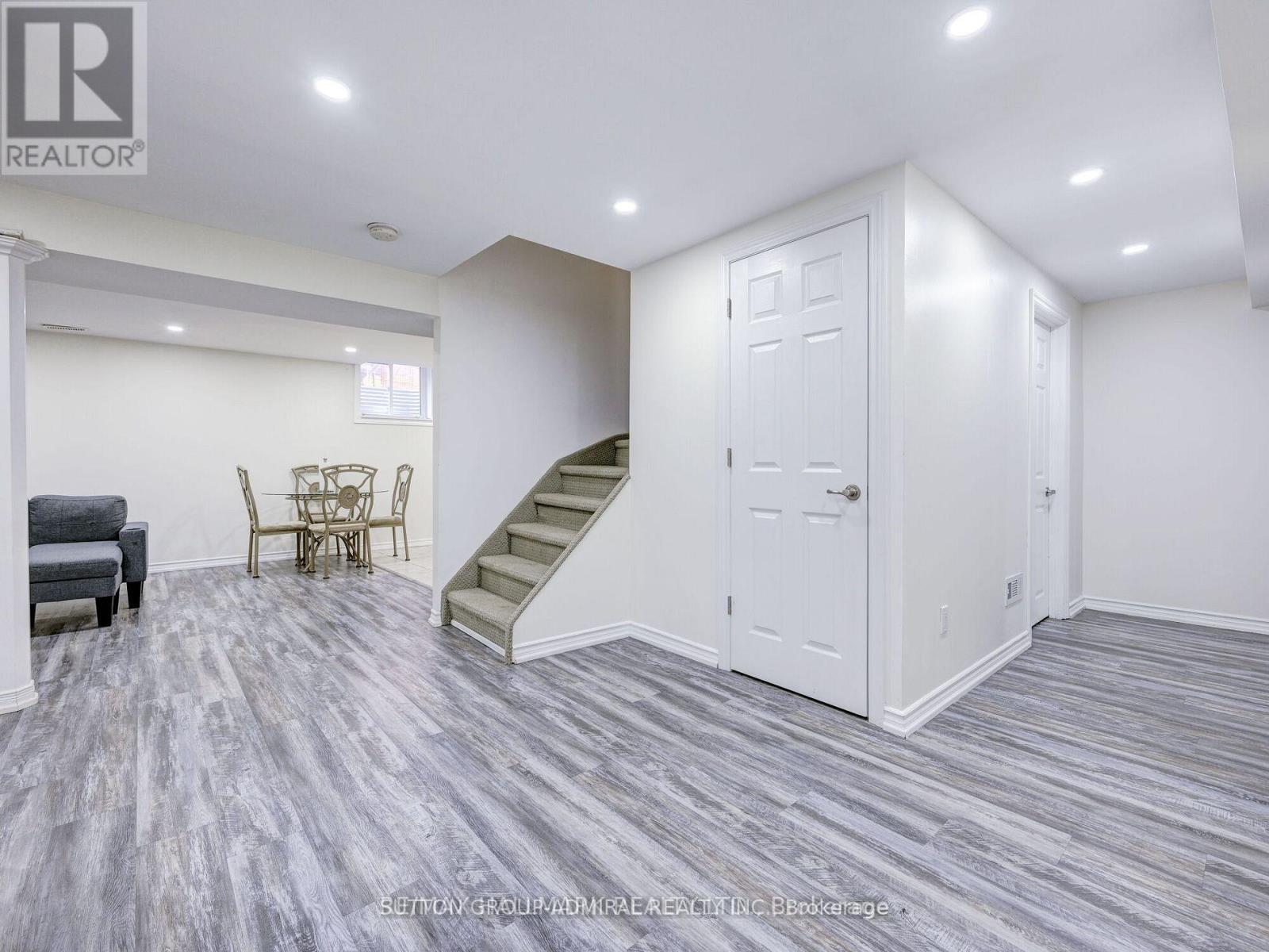 A living room with a grey carpet and a staircase.