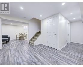 A living room with a grey carpet and a staircase.
