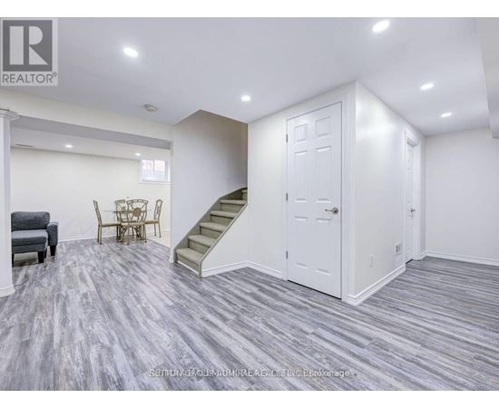 A living room with a grey carpet and a staircase.
