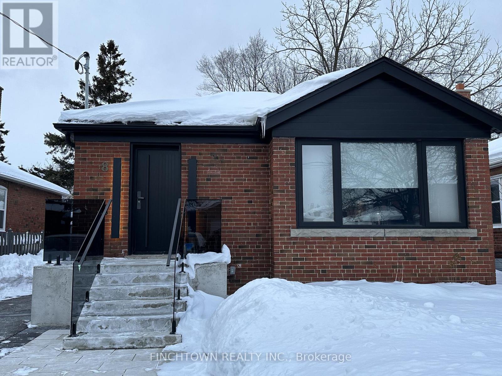 A house with a black door and windows is surrounded by snow.