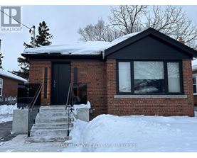 A house with a black door and windows is surrounded by snow.