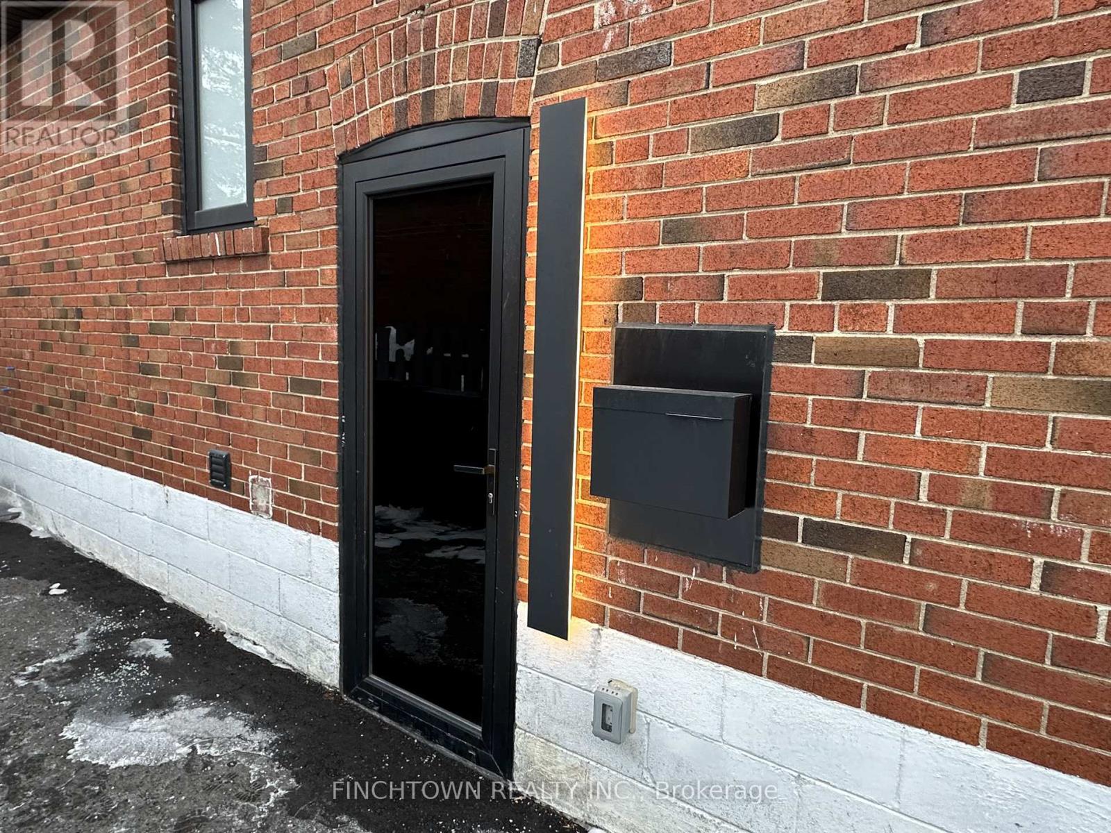 A black door is on the left side of a brick wall.