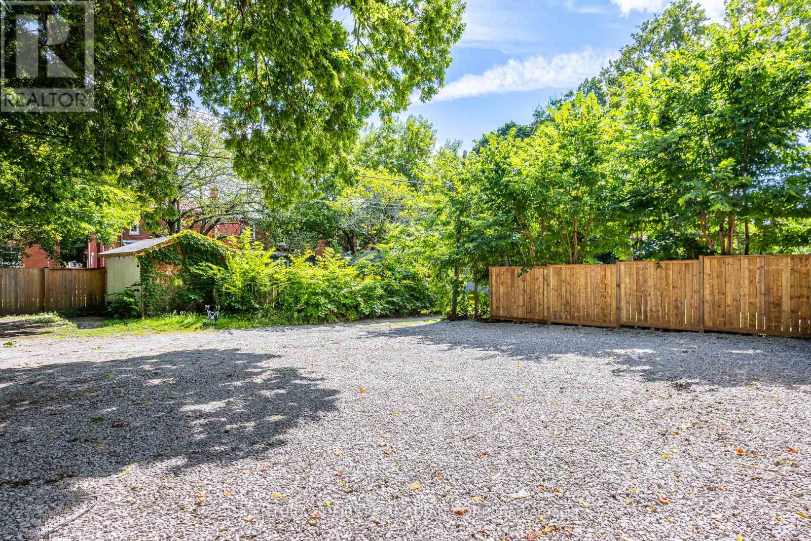 A gravel driveway leads to a wooden fence and green trees.
