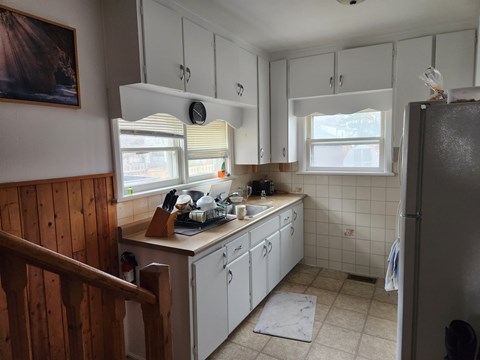 A kitchen with white cabinets and a wooden staircase.