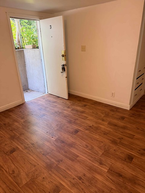 A room with a wooden floor and a door leading outside.