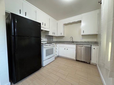 A black refrigerator stands in a kitchen with white cabinets and a granite countertop.