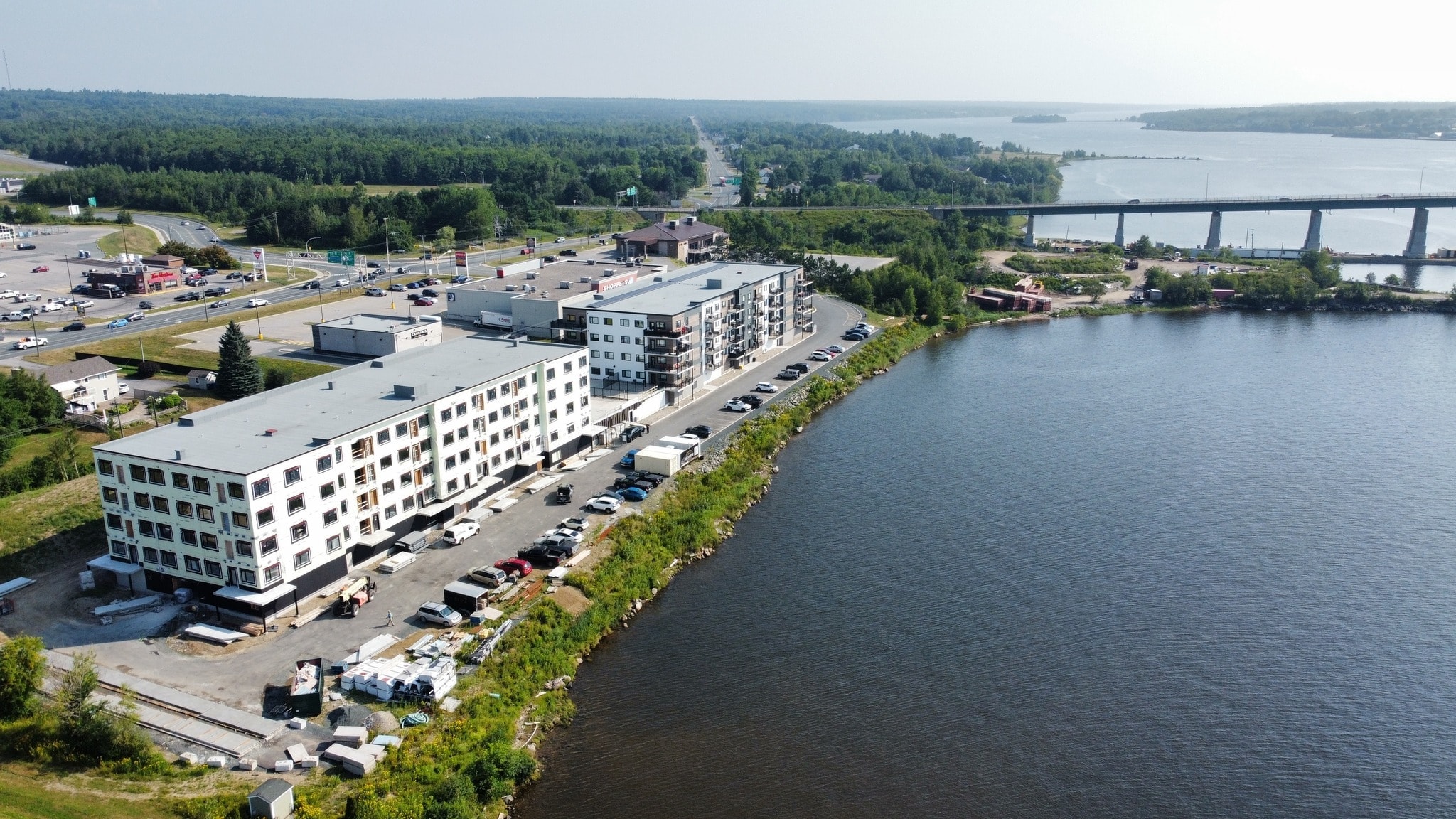 A large white building sits next to a body of water with a bridge in the background.