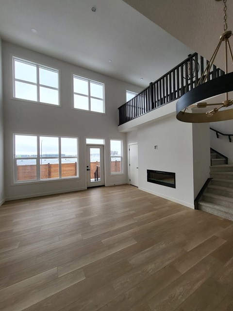 A large, empty room with wooden floors and a staircase with a black railing.
