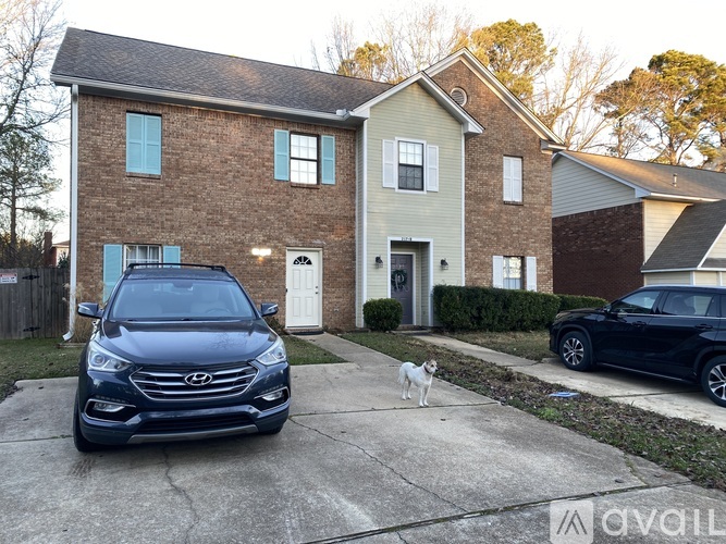 A black SUV is parked in front of a two-story house with a white dog standing on the concrete driveway.