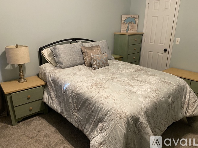 A bed with a white comforter and a green nightstand with a lamp on it.