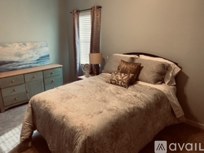 A bedroom with a bed, nightstand, and a painting of a beach scene.