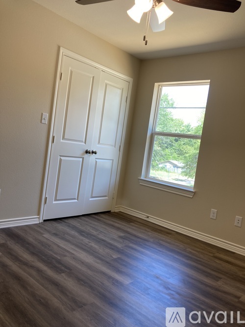 A room with a white door and a window with a view of trees outside.