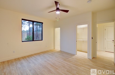 A room with a ceiling fan and a window overlooking a forest.