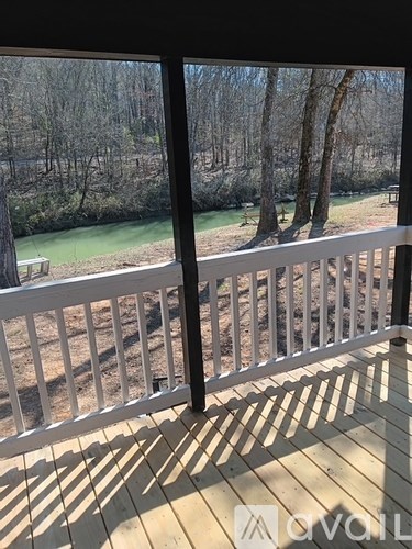 A deck with a white railing overlooks a wooded area and a body of water.
