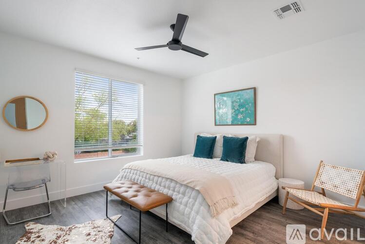 A bedroom with a large bed, a ceiling fan, and a window with blinds.