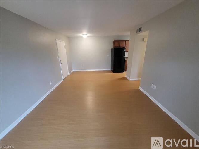 A spacious room with wooden flooring and a black refrigerator.