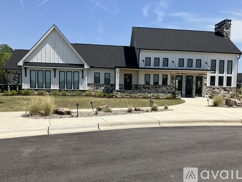 A large white building with a black roof and a stone chimney is surrounded by a landscaped area with rocks and plants.