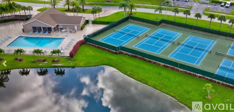 A tennis court is surrounded by a grassy area and a pool.