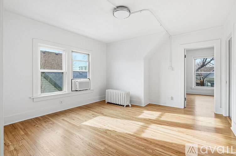 A room with wooden floors and white walls, with a window showing a view of a building and a tree.