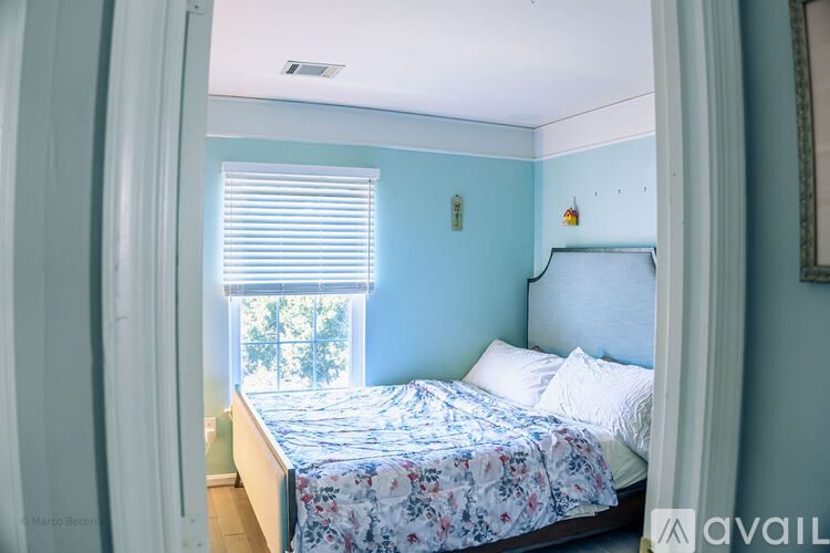 A bedroom with a bed, a window with blinds, and a mirror on the wall.