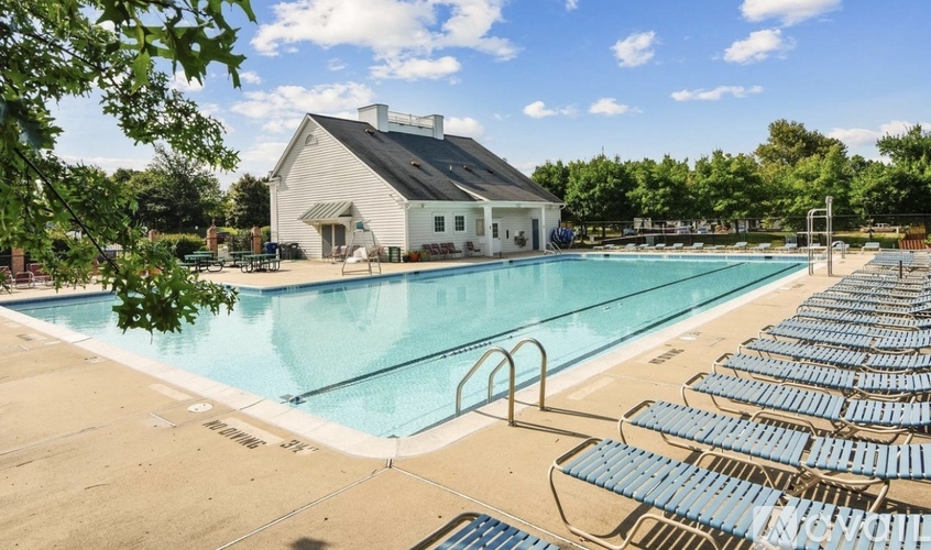 A large outdoor swimming pool with blue seats and a white building in the background.