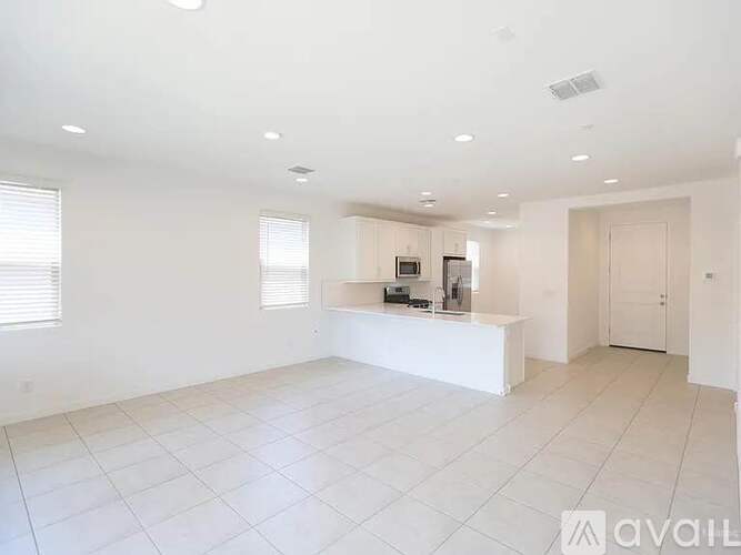 A spacious, empty room with white tiled flooring and a counter with a microwave and coffee maker.