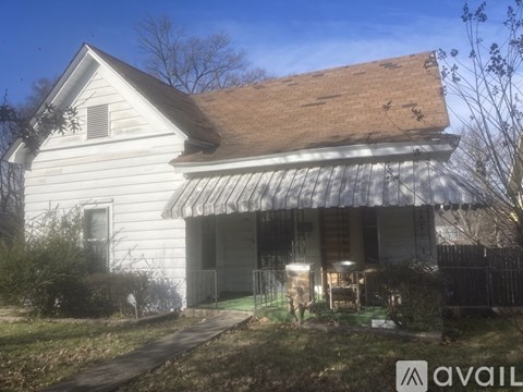 A white house with a brown roof and a metal awning is for sale.