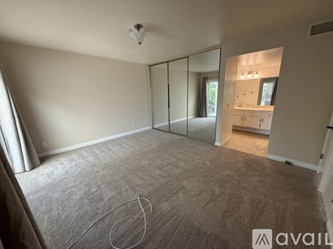 A spacious room with wooden flooring and a staircase in the background.