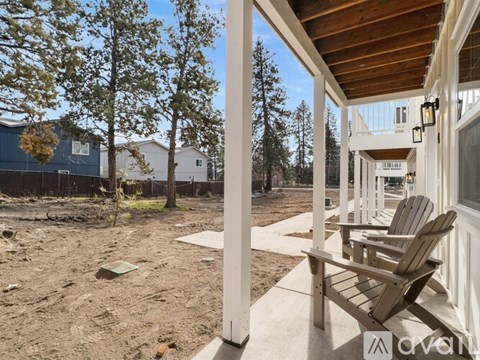 A wooden bench is on a porch with a view of a backyard.