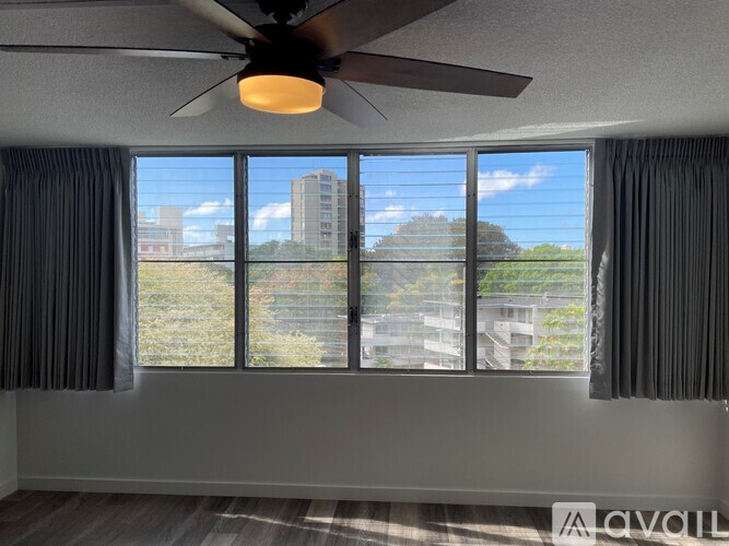 A room with a ceiling fan and a window showing a view of a building and trees.