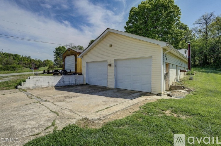 A two-car garage is situated in a grassy area with a house in the background.