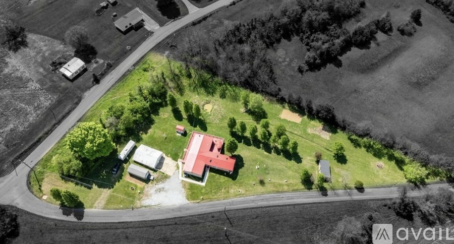 A bird's eye view of a house with a red roof surrounded by trees and a road.