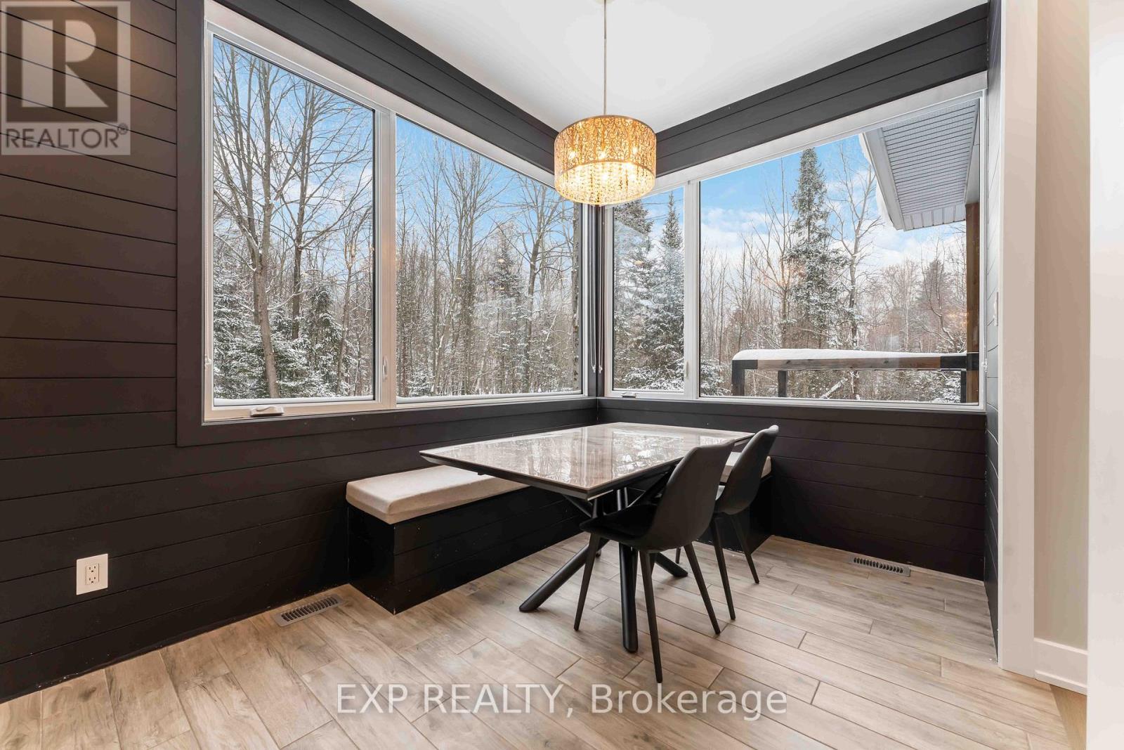 A dining room with a table and chairs and a view of trees outside the window.