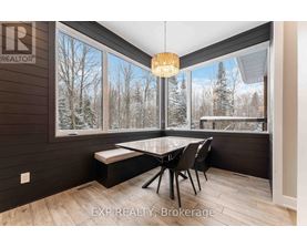 A dining room with a table and chairs and a view of trees outside the window.