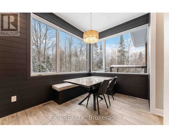 A dining room with a table and chairs and a view of trees outside the window.
