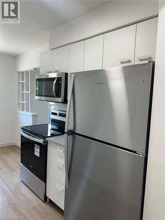 A stainless steel refrigerator stands in a kitchen with white cabinets and a microwave above the oven.