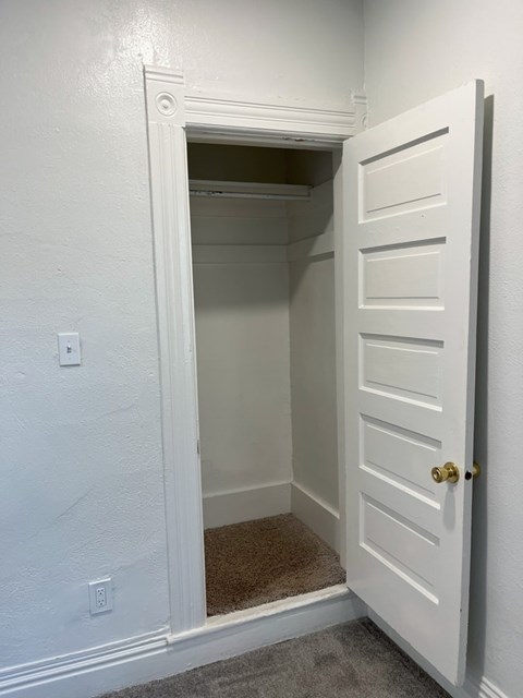A white door with a gold handle is open to a small, empty room.