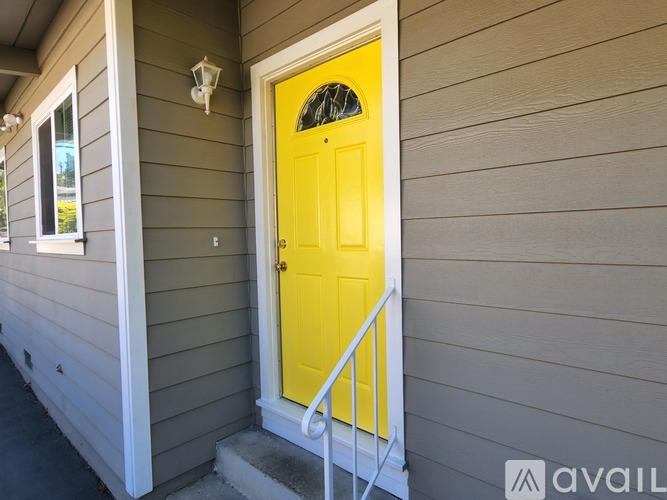 A yellow door is on the right side of a grey house.