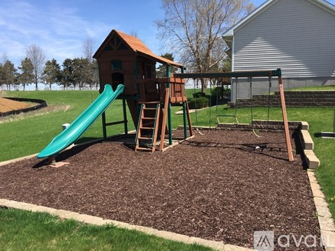 A playground with a green slide and a wooden playhouse.