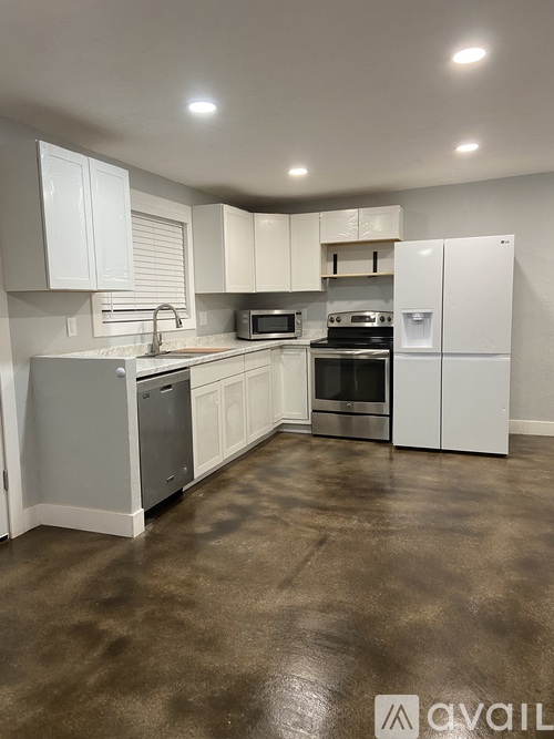 A kitchen with white cabinets and brown flooring.