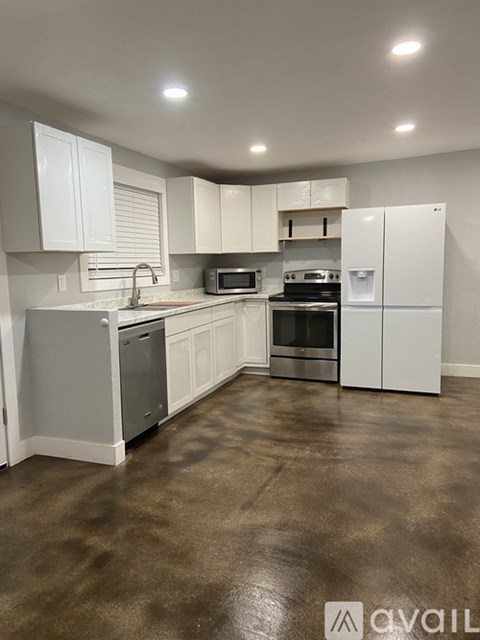 A kitchen with white cabinets and brown flooring.